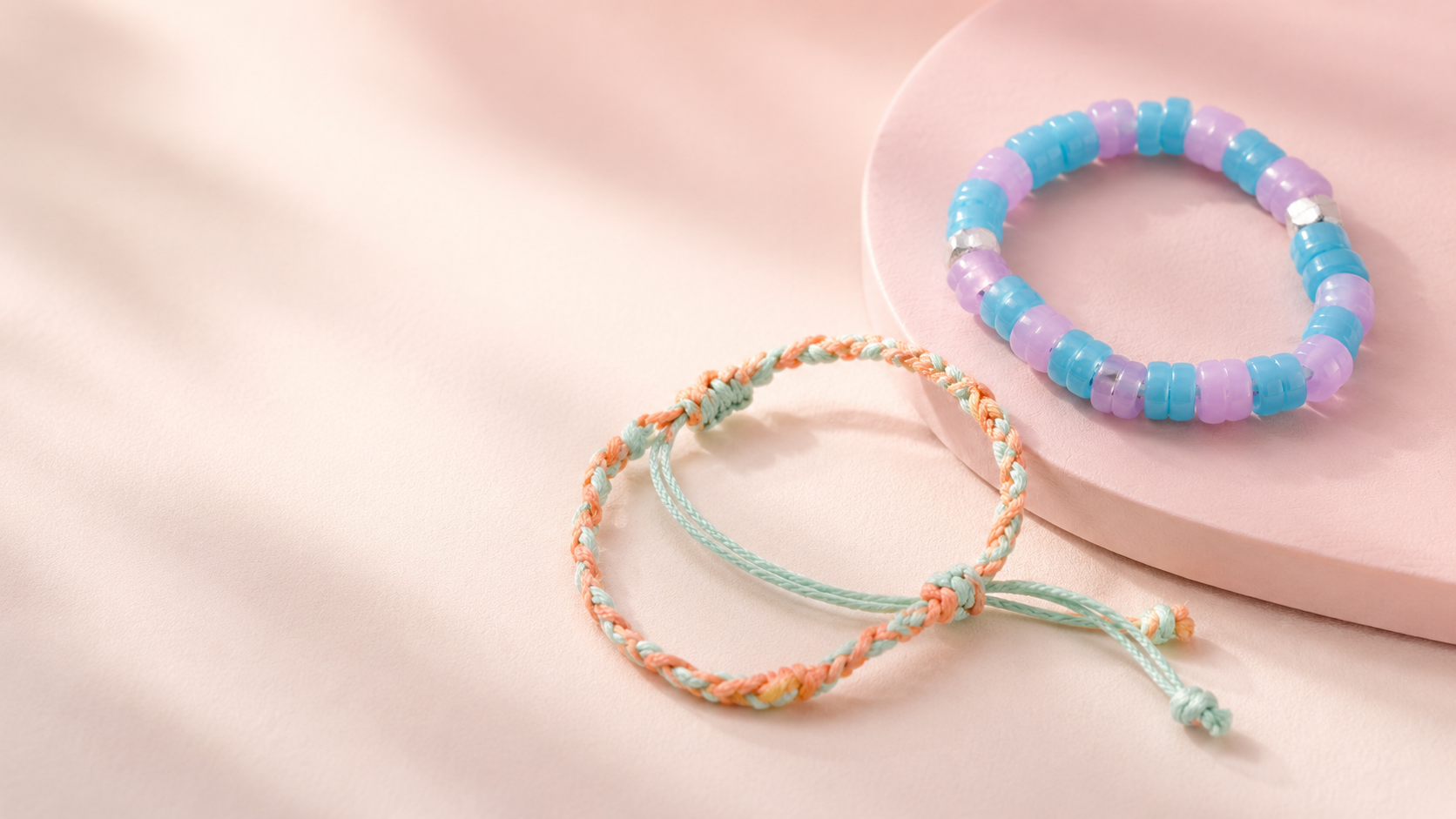 Pastel beaded and braided bracelets arranged on a pink platform